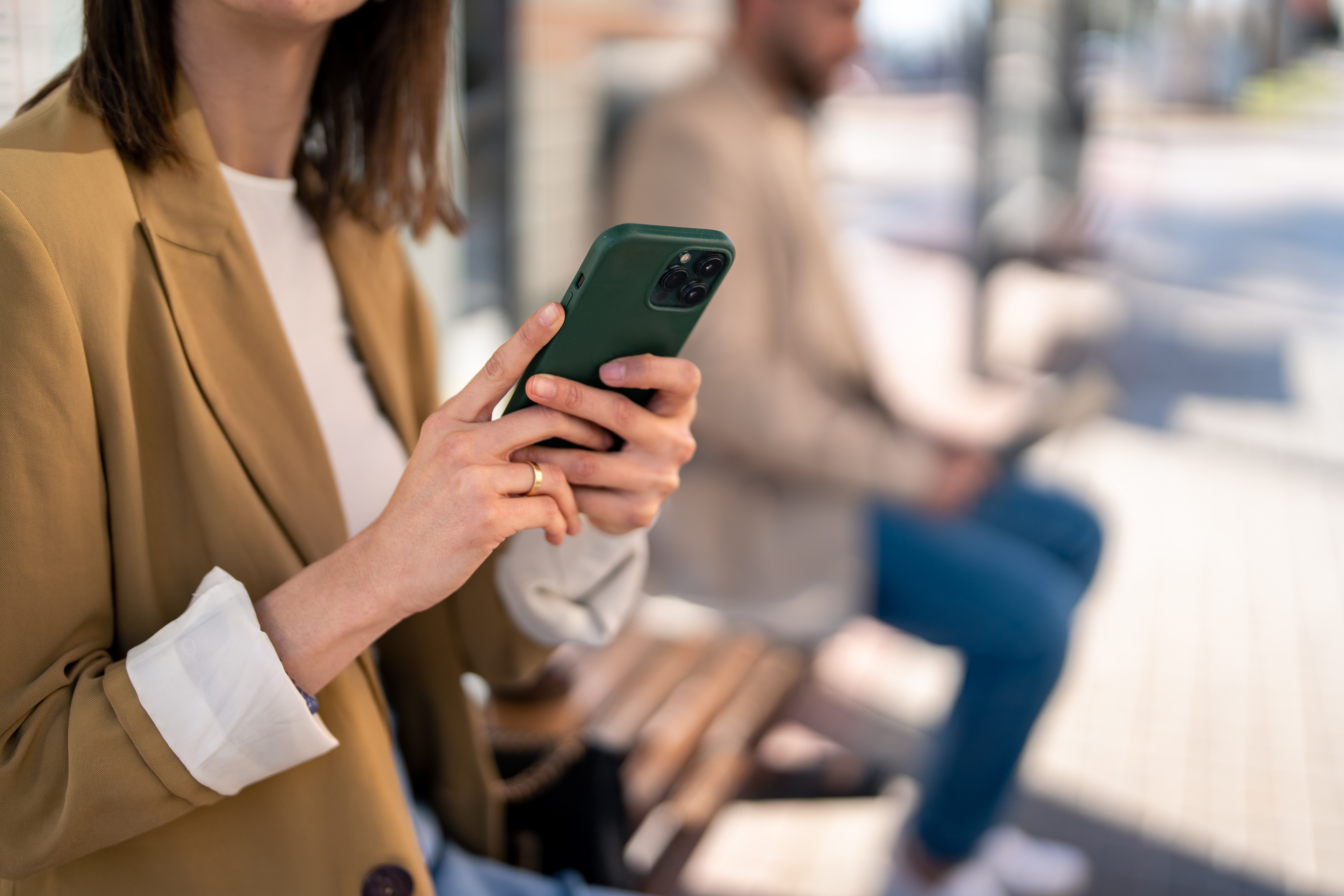 Hands of unrecognizable woman holding mobile phone while sitting at bus station and waiting for bus, using smart phone to check bus schedules, connections, routes and maps, buying bus ticket on online app.